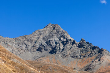 Impregnable granite black steep mountainside and sharp rocks with top peak under background of clear blue sky. Gran Paradiso National Park. Aosta valley, Italy