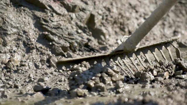 Builder levelling and spreading concrete with a rake in close up slow motion view.