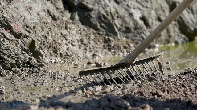 Builder levelling and spreading concrete with a rake in close up slow motion view.