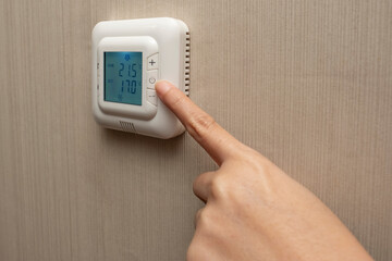 Adjustment, energy and power consumption concept. Close up of hand setting room temperature on thermostat at hotel. Brown wallpaper as background.