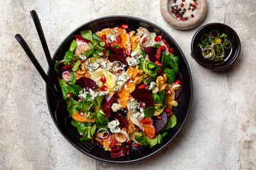 Winter salad with beetroot, oranges, walnuts, pomegranate, dried cranberries, valerian lettuce,  iceberg, onion and blue cheese. Healthy eating. Honey and olive oil dresseng. Above, light background.