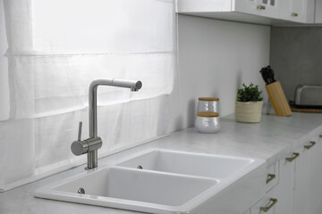Fototapeta na wymiar Modern sink and water tap near window in kitchen. Interior design