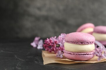 Obraz na płótnie Canvas Delicious violet macaron and lilac flowers on black table, closeup. Space for text