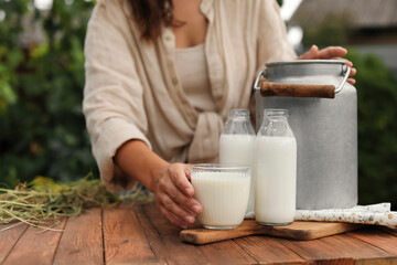 Woman taking glass with fresh milk at wooden table outdoors, closeup