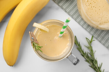Mason jar of tasty banana smoothie with straw and fresh fruits on white marble table, flat lay