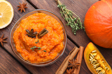 Bowl of delicious pumpkin jam and ingredients on wooden table, flat lay