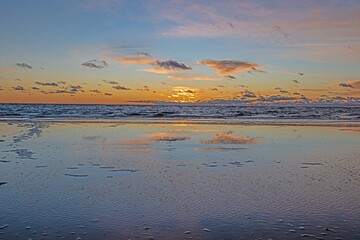 Obraz premium Sunset over the sea with reflections in the rising surf