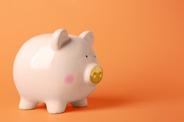 Ceramic piggy bank on orange background. Space for text