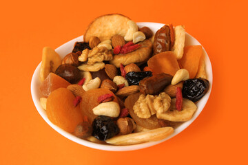 Bowl with mixed dried fruits and nuts on orange background, closeup
