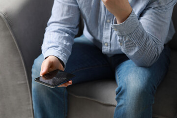 Man holding damaged smartphone while sitting on armchair, closeup. Device repairing