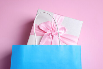 Light blue paper shopping bag with gift box on pink background, top view