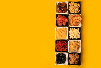 Bowls with dried fruits and nuts on yellow background, flat lay. Space for text