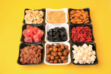 Bowls with dried fruits and nuts on yellow background