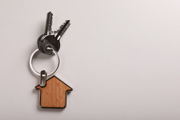 Keys with trinket in shape of house on white background, top view and space for text. Real estate agent services