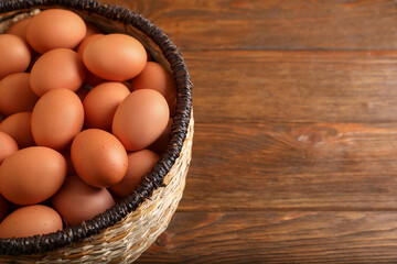 Raw chicken eggs in wicker basket on wooden table, space for text