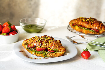 Sweet croissant sandwiches with pistachio cream, strawberries and caramel dip on white wooden table and grey bckground