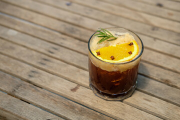 A glass of coffee with orange and rosemary on top, on the wooden table
