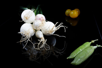 a couple of fresh onions with roots and green leafs presented on a black background.