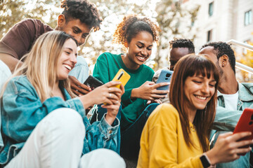 Group of multiracial young people using smart mobile phone device outdoors - Happy university students watching cellphones sitting in college campus - Teenagers addicted to social media technology