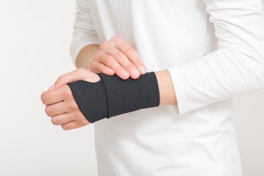 Young adult woman hand with protective black elastic wrist bandage isolated on light gray background. Closeup. Side view.