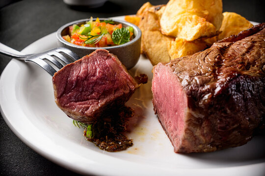 Propuesta gastronomica gourmet, lo mejor de la carne argentina. Bife de chorizo "a punto" servido directamente por las manos del chef, emplatado con acompa&ntilde;amientos y sobre una mesa de mantel negro. 
