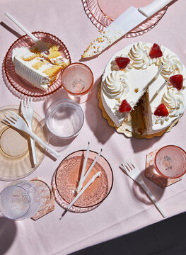 White birthday cake with strawberries and candles on pink tablecloth
