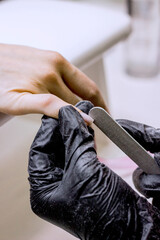 Manicurist saws nails with a nail file and shaped nails during the nail extension procedure or manicure in a beauty salon. Professional hand care in salon