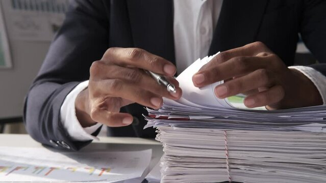 Businessman hands working in Stacks of paper files for searching information on work desk home office, business report papers, piles of unfinished documents achieves with clips indoor.