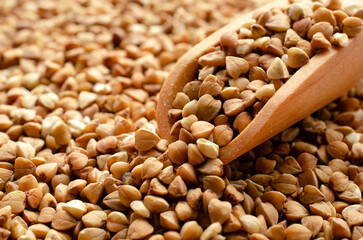 Heap of buckwheat seeds with a wooden spoon, close-up, top view. Close-up of buckwheat seeds with wooden spoon, background. Pile of buckwheat seeds with wooden spoon, background, top view.