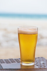 Glass of cold beer with foam on the table. Against on background of the blue sea. 