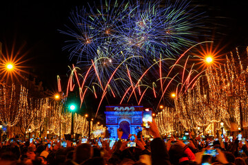 Paris, France - January 1st, 2023 : New Year's fireworks over the Arc de Triomphe (triumphal arch) on the Champs Elysées in Paris to celebrate the passing to 2023 on front of a large crowd