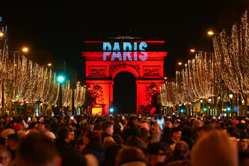 Paris, France - January 1st, 2023 : Crowd gathered on the Champs Elysées in Paris to celebrate the passing to 2023 with a fireworks show over the Arc de Triomphe (triumphal arch)