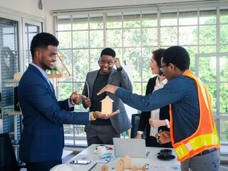 Businesspeople's multiracial colleagues brainstorm with house models and blueprints at the office. Professional construction team discussing the arrangement of service lines at the new building..