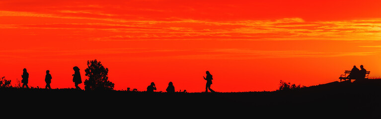 Silhouette of young people in sunset with beautiful orange sky in background, youth lifestyle and fun concept