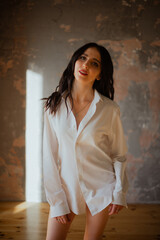 Sexy young brunette girl in a white shirt and lingerie in a loft photo studio