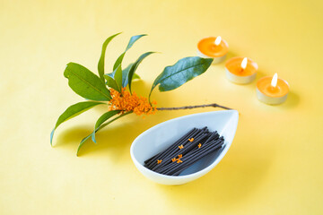 金木犀の香りのミニ寸の線香と小さな金木犀の花（オレンジ色の背景）