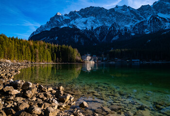 “Eibsee“ is an alpine Lake with crystal clear turquoise water underneath the highest summit of Germany the “Zugspitze“ near Garmisch-Partenkirchen Bavaria. Cable car going up to 2.962 m high peak. - obrazy, fototapety, plakaty