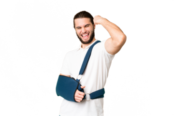 Young handsome man with broken arm and wearing a sling over isolated chroma key background celebrating a victory