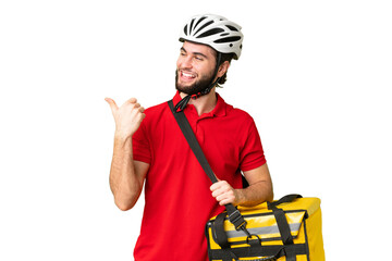 Young delivery man with thermal backpack over isolated chroma key background pointing to the side to present a product