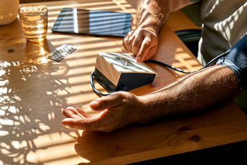 Middle aged man measuring his arterial blood pressure in the morning, using blood-pressure cuff to...
