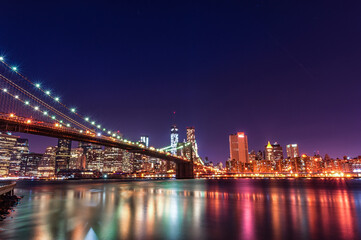 Fototapeta na wymiar Brooklyn Bridge at Night. Long Exposure. New York. NYC, USA. Lights Reflection on Water.