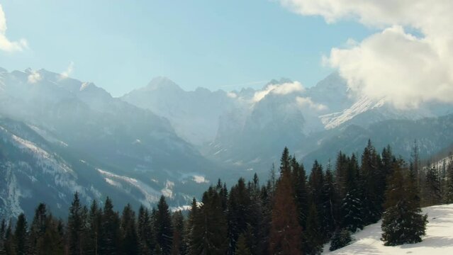 Epic Mountains Aerial B-roll with Peak Range and Pine Woods and Forest in Snow. Scenic Landscape in Sunny Winter Day with Trees, Clouds and Blue Sky. 4K Background Drone Pan left Shot in Tatra, Poland