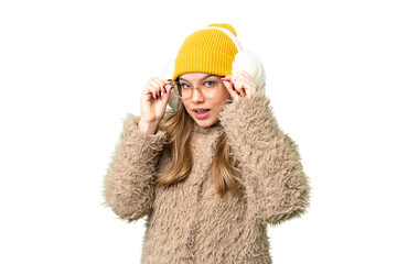 Young girl wearing winter muffs over isolated chroma key background with glasses and surprised