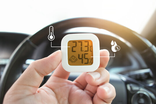 Thermometer and humidity instrument with temperature and humidity symbol holding by driver hand in a car