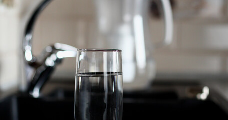 A glass of water is on the table, with a filter jug and a kitchen faucet in the background. The...