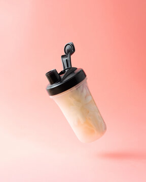 Protein shaker bottle in air.Filled with flowers against soft pink background. Creative gym or workout concept.