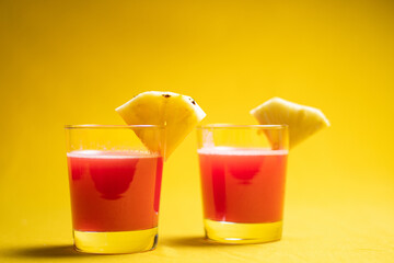 Pineapple juice in glass closeup near sliced fruit with spash and dripping liqid for summer vibes.