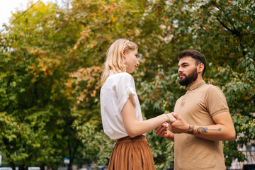 Shooting from below of pretty young couple in love standing at city park and looking at each other with falling in love eyes. Bearded handsome man and blonde woman walking spending time together