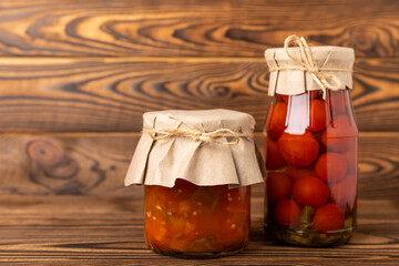 Lecho salad and pickled tomatoes in a glass jar on a textured table. Vegetable salads and pickles in glass jars. Homemade preserves. Preservation and storage of products. Place for text. Copy space.