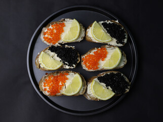 delicious fragrant sandwiches or bruschetta with melted cheese and black caviar and red caviar and lemon on a dark background. for splash screens labels flyers menu banners